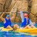 A man and a woman smile while kayaking through the water next to a rock formation